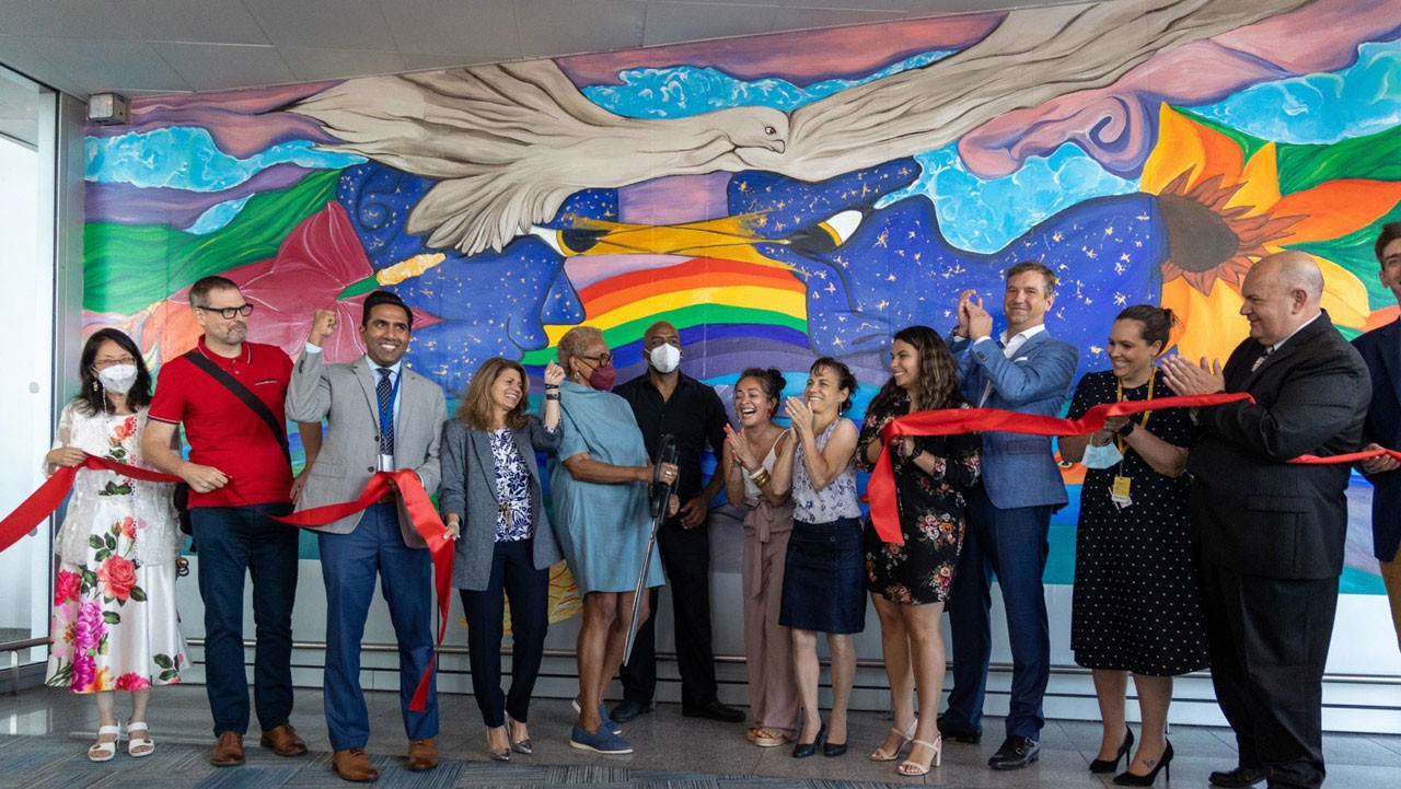 A group of people celebrating a ribbon-cutting event in front of a vibrant mural.